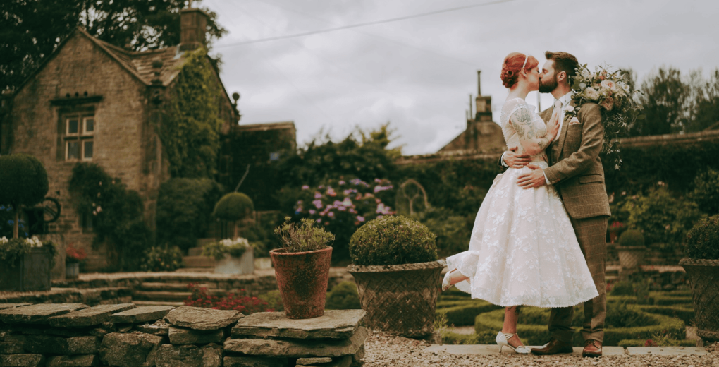 A bride and groom sharing an intimate kiss in the charming gardens of Holdsworth House, a venue for small weddings in Halifax.
