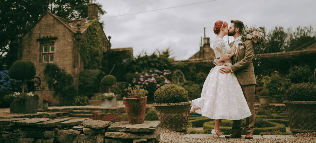 A bride and groom sharing an intimate kiss in the charming gardens of Holdsworth House, a venue for small weddings in Halifax.