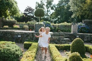Children playing among neatly trimmed hedges and stone pathways in the formal gardens of Holdsworth House. credit: ©Tim Dunk Photography