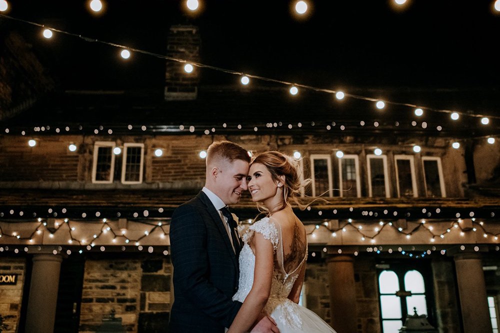 Bride and groom share a romantic moment under twinkling string lights in the courtyard at Holdsworth House