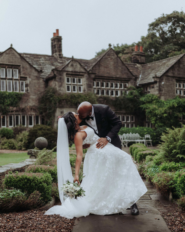 A bride and groom share a romantic dip and kiss in front of Holdsworth House, a historic wedding venue in Halifax