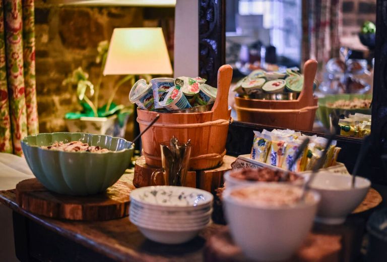 A cosy breakfast buffet spread with bowls of cereal, yogurt cups, and various condiments displayed on a rustic wooden table.