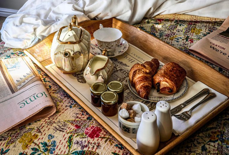 Breakfast tray with tea, croissants, and preserves on a colourful quilt at Holdsworth House.