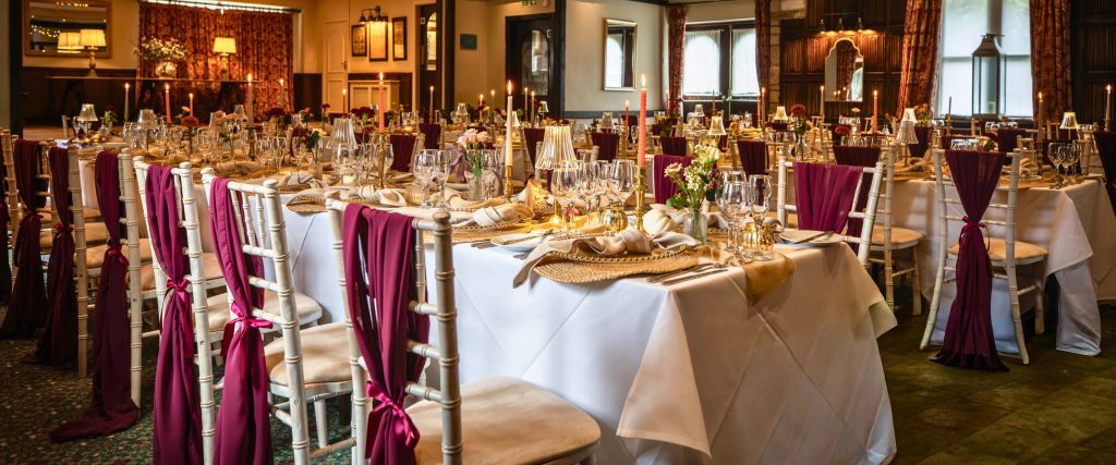 Wedding breakfast room at Holdsworth House set with gold and burgundy décor, candles and floral arrangements.
