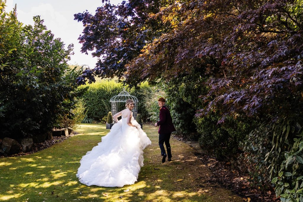 Wedding couple walking through the grounds near the birdcage at Holdsworth House.