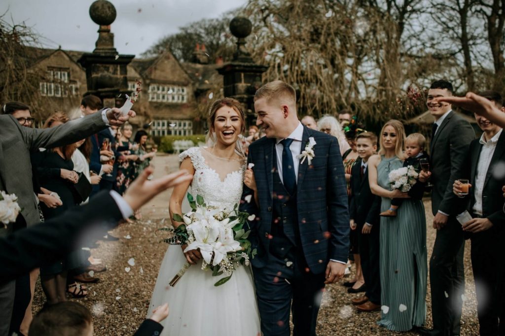Wedding couple walking through confetti with guests at Holdsworth House.
