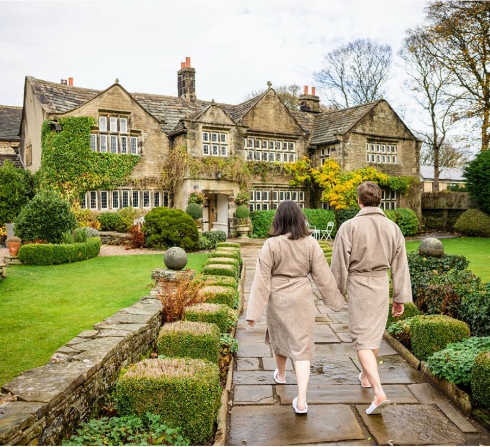 Couple enjoying a Valentine’s spa break at Holdsworth House, walking through the gardens in bathrobes.