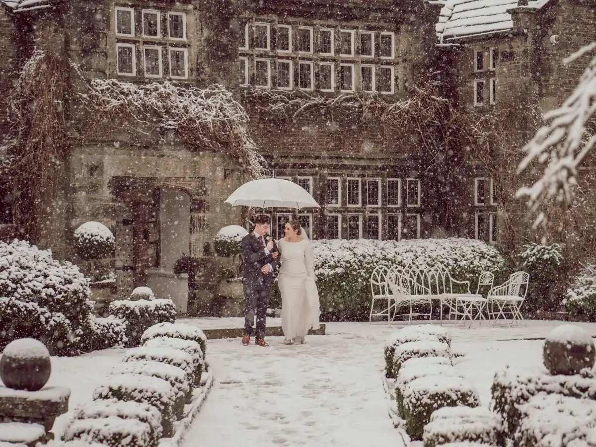 A winter wedding couple at the snowy gates of Holdsworth House
