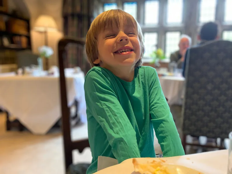 A boy grinning over his afternoon tea in the restaurant at Holdsworth House, Halifax