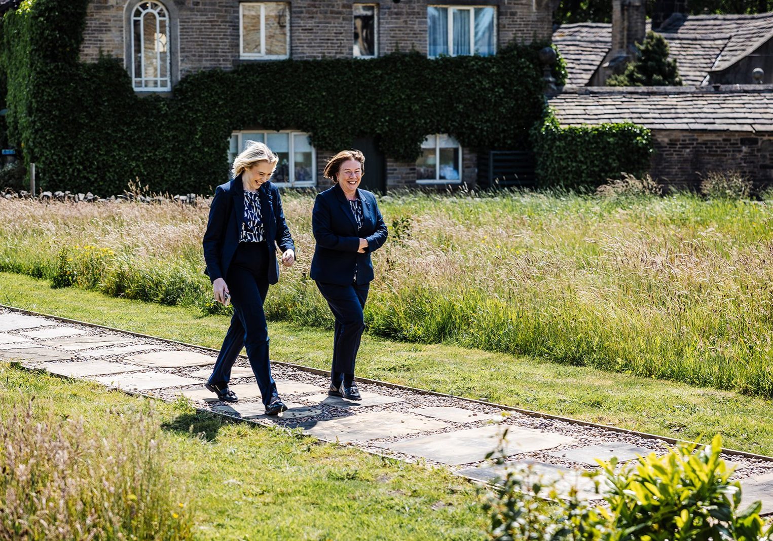 Claire and Ruby wedding coordinators walking across the paddock to the barn courtyard at Holdsworth House